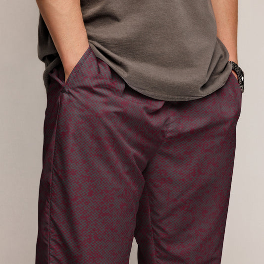 Person wearing maroon patterned track pants and a gray shirt against a neutral background