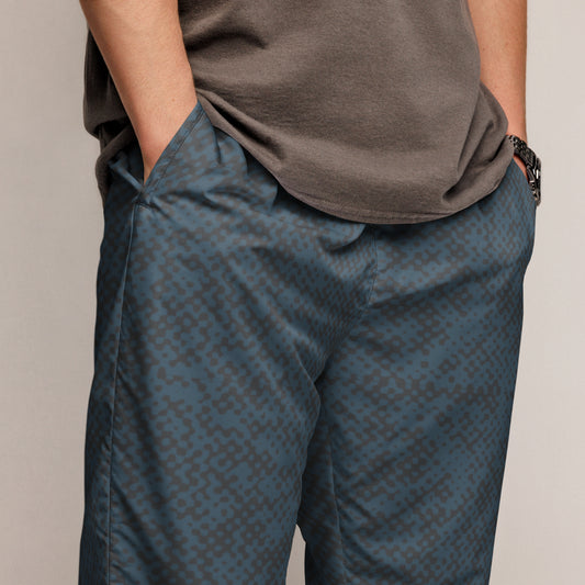 Person wearing a patterned blue track pants and brown shirt on a plain background