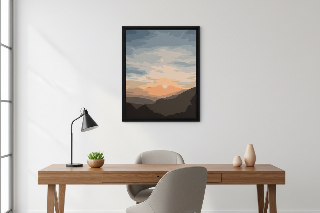 Framed artwork of a sunset over mountains on a wall above a desk.