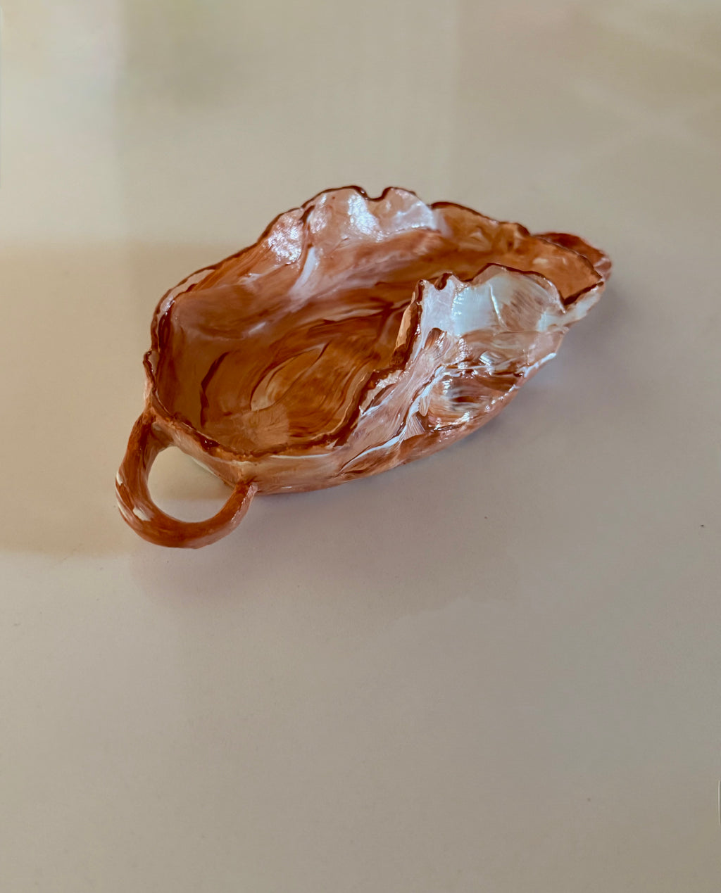 A small leaf-shaped ceramic dish with a handle, featuring a glossy burnt orange and white marbled glaze