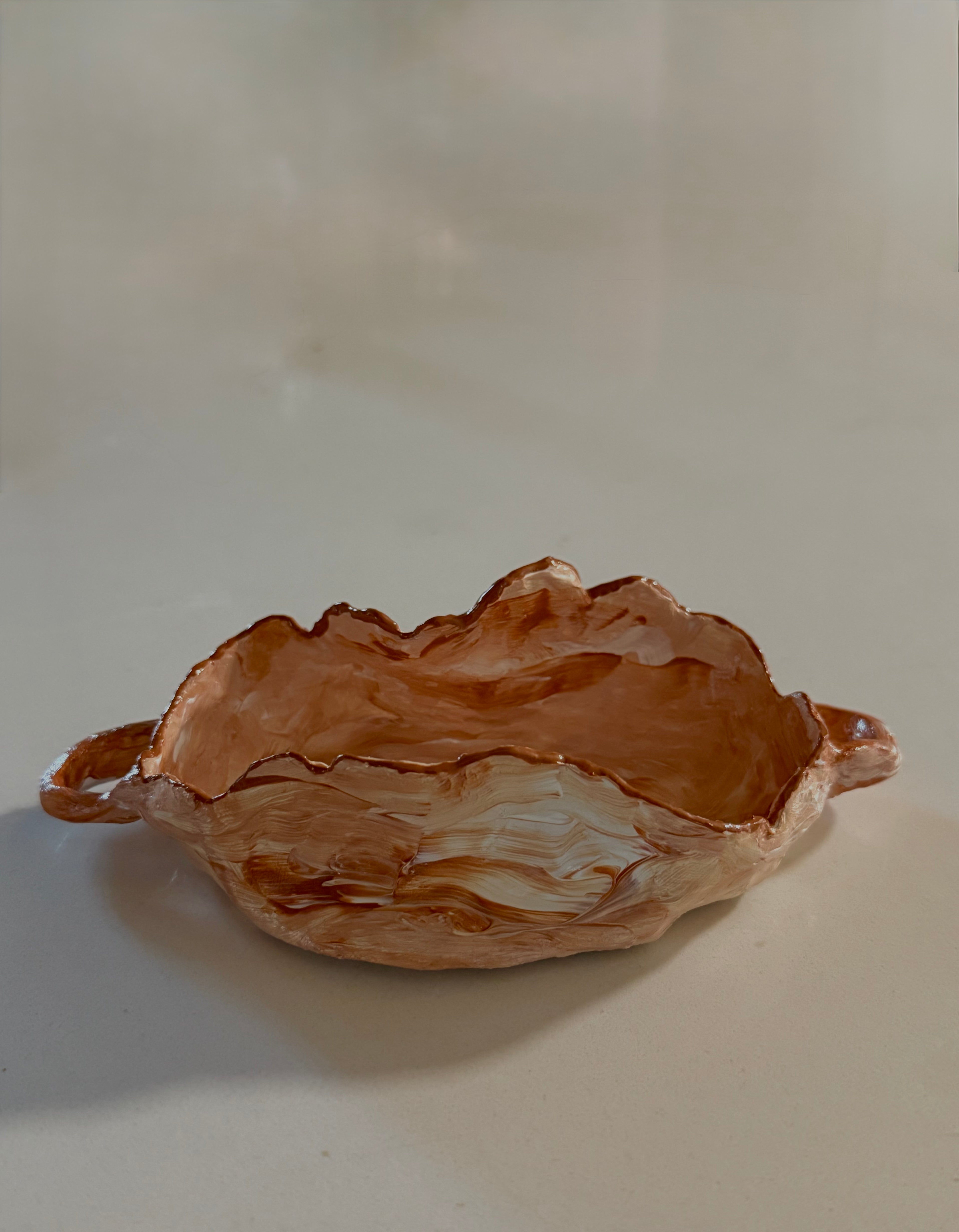 A handmade ceramic bowl with a textured, organic leaf-like rim and small side handles