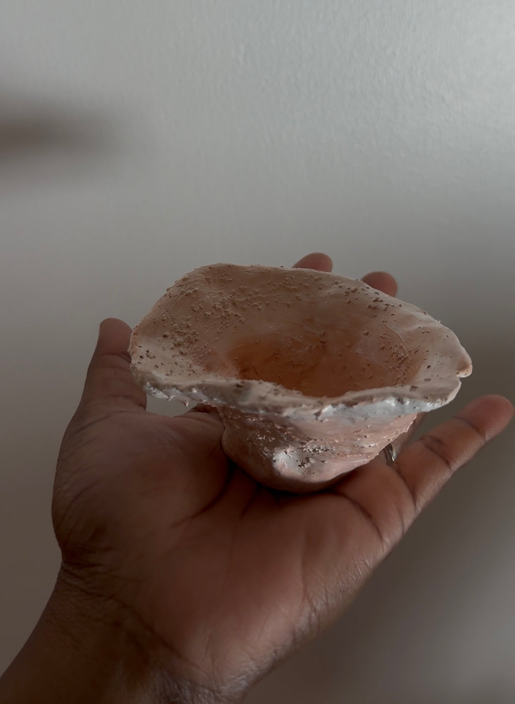 A hand holding a small, organic-shaped decorative textured bowl
