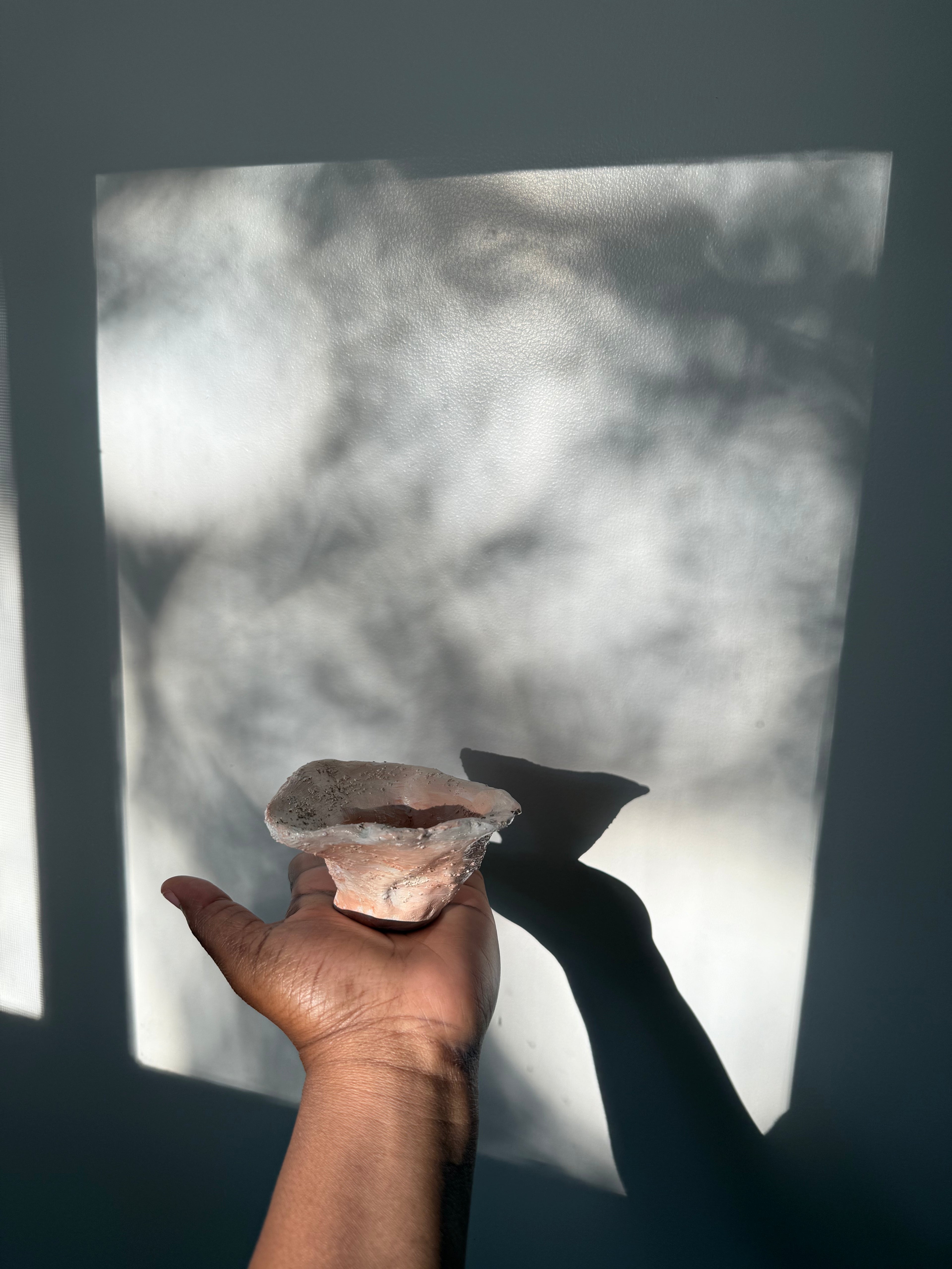 A hand holds a small, rustic, terracotta and cream ceramic catchall bowl for jewelry 