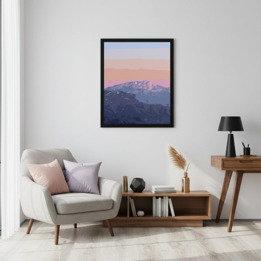 Framed mountain landscape print on a wall above a chair with cushions in a living room setting.