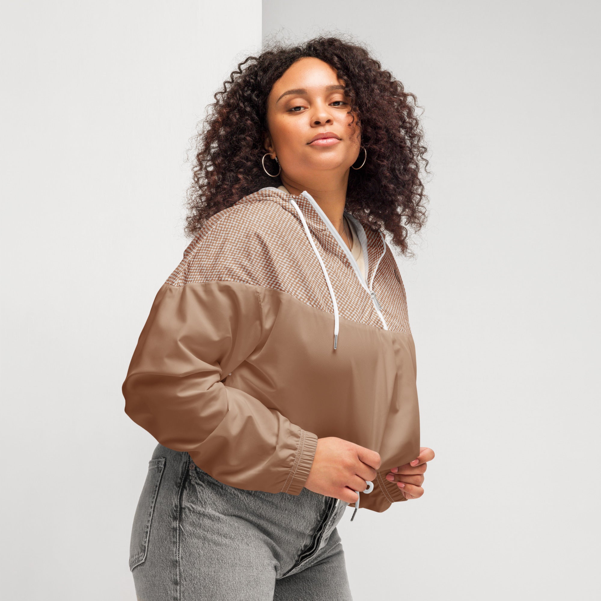 Woman wearing a brown windbreaker jacket and gray jeans against a plain background