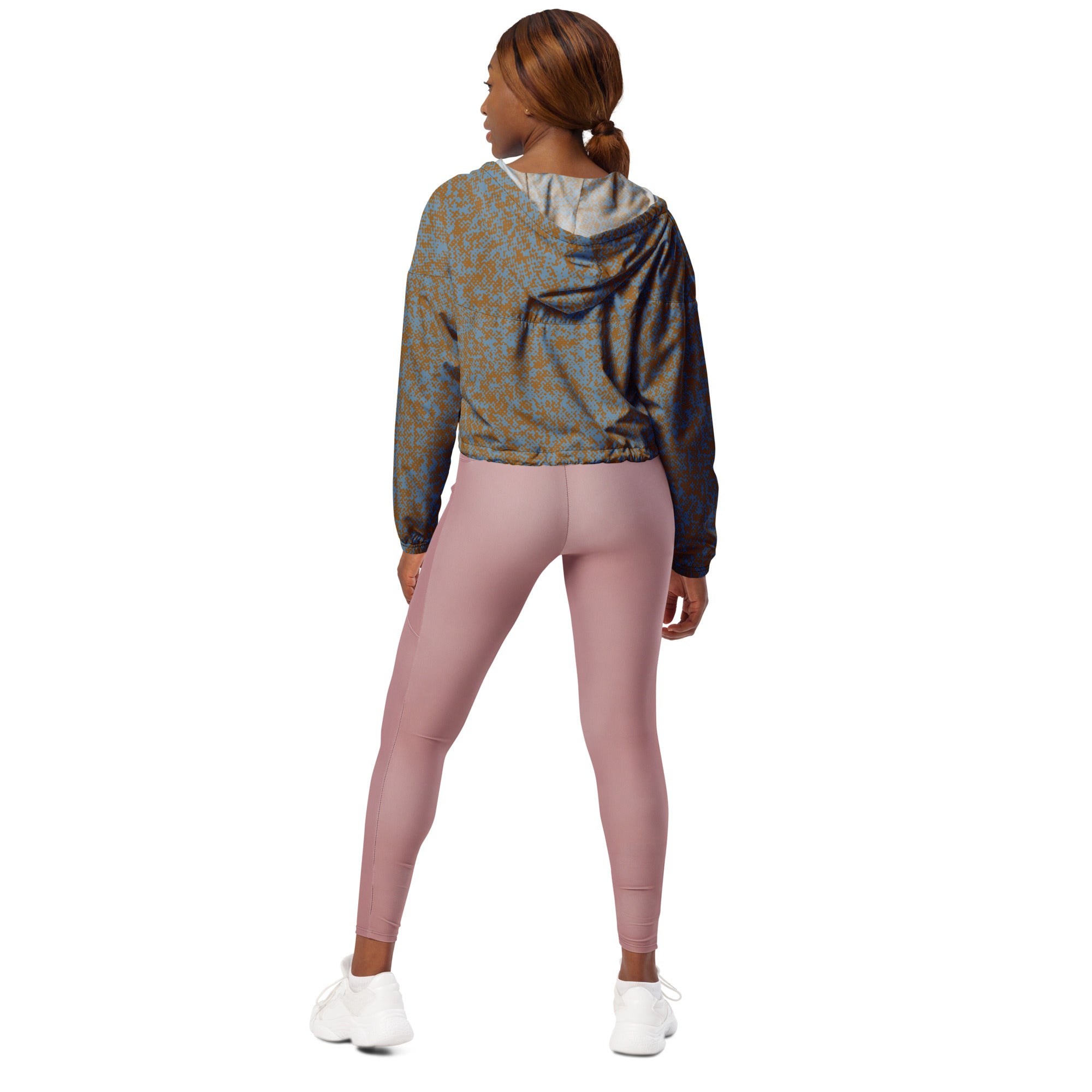 Back view of woman wearing a patterned windbreaker jacket hoodie and pink leggings on a white background