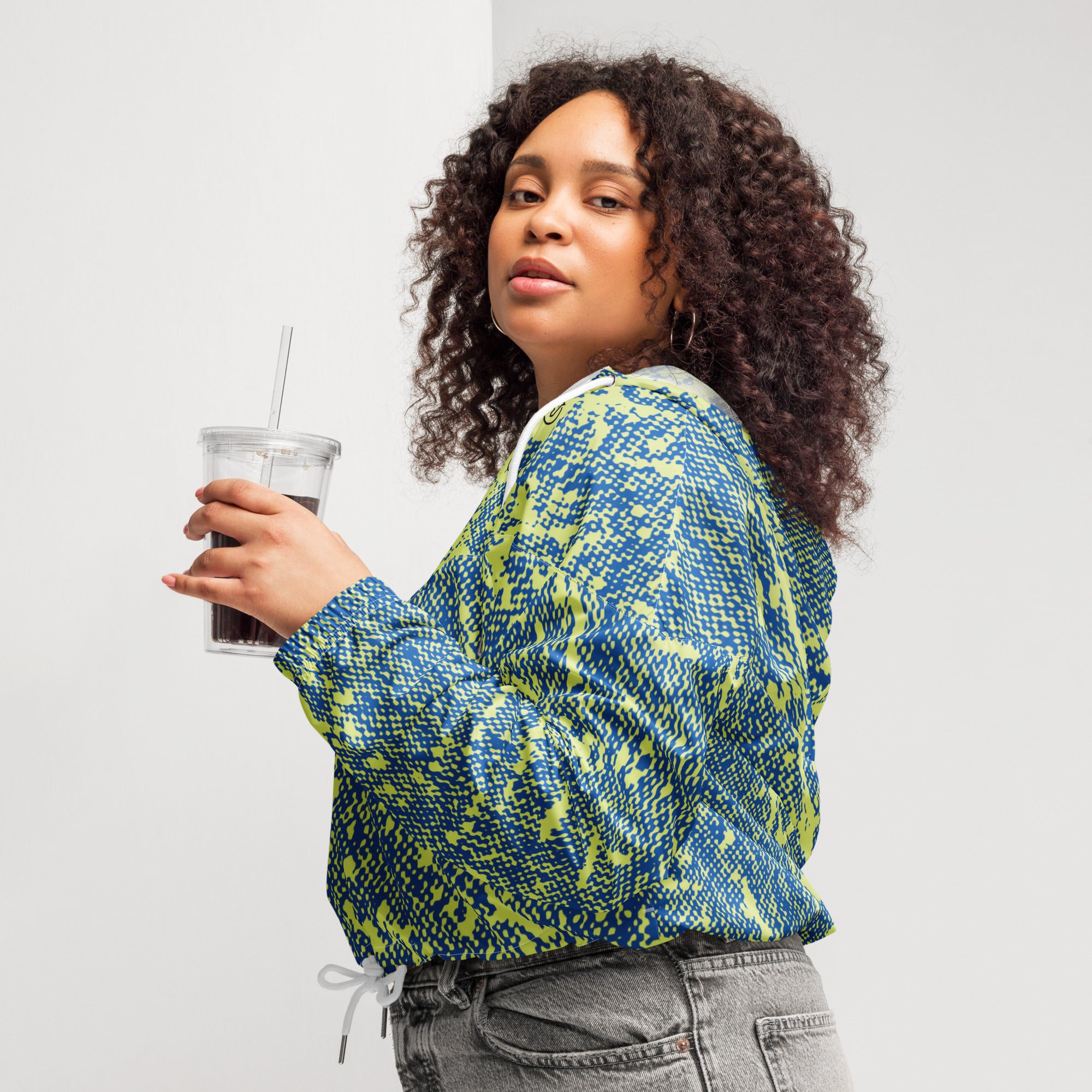 Woman in blue and green patterned windbreaker jacket holding a drink