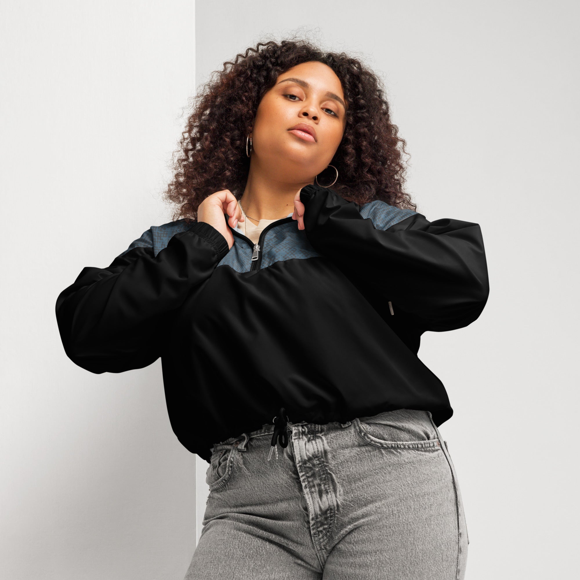 Woman wearing a black and navy windbreaker jacket and gray jeans against a plain background