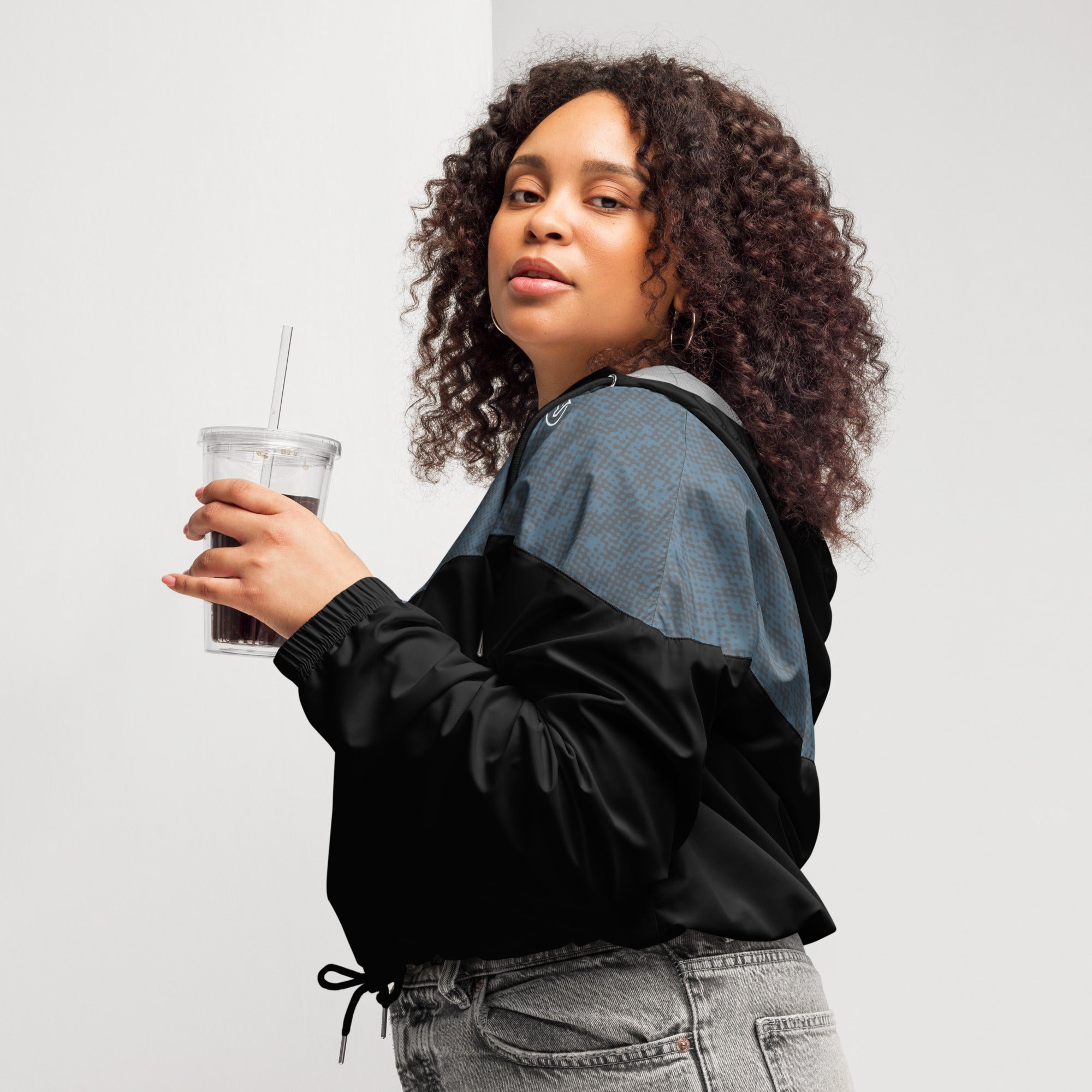 Woman wearing a navy blue and black windbreaker jacket holding a drink with a straw against a plain background
