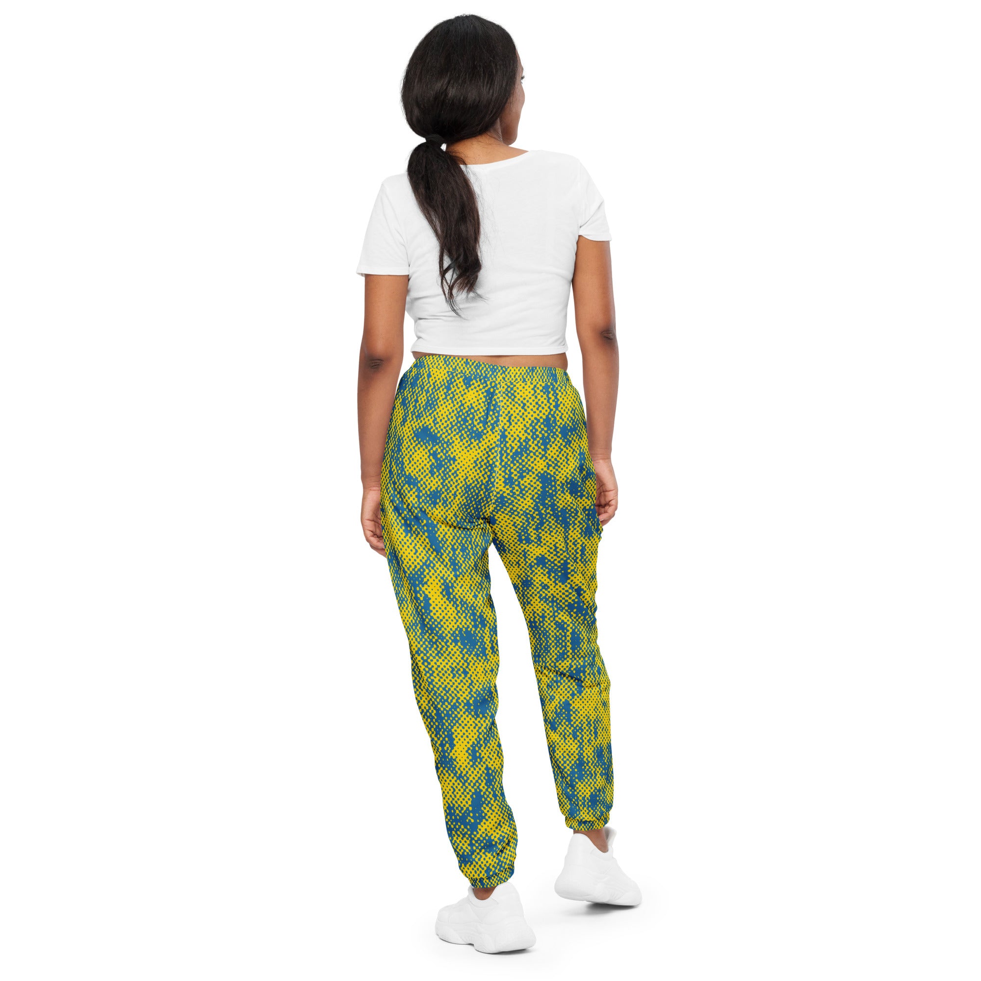 back view of woman wearing a white crop top and colorful patterned track pants on a white background