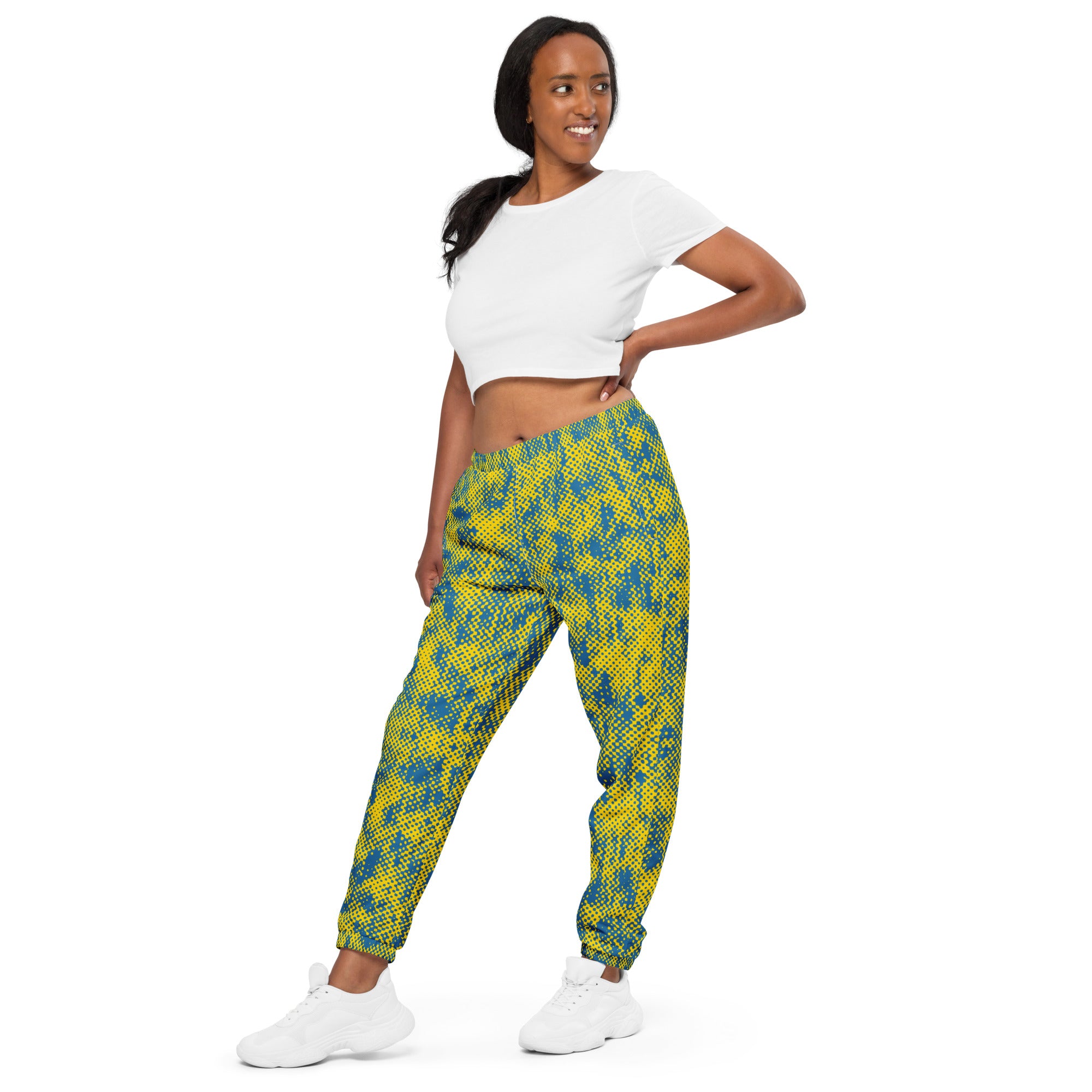 Woman wearing a white crop top and yellow and blue patterned track pants on a white background