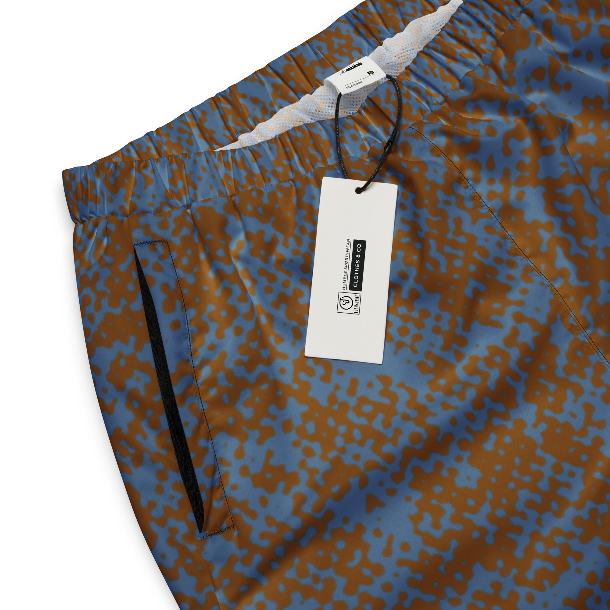 Blue and brown patterned track pants with a tag on a white background