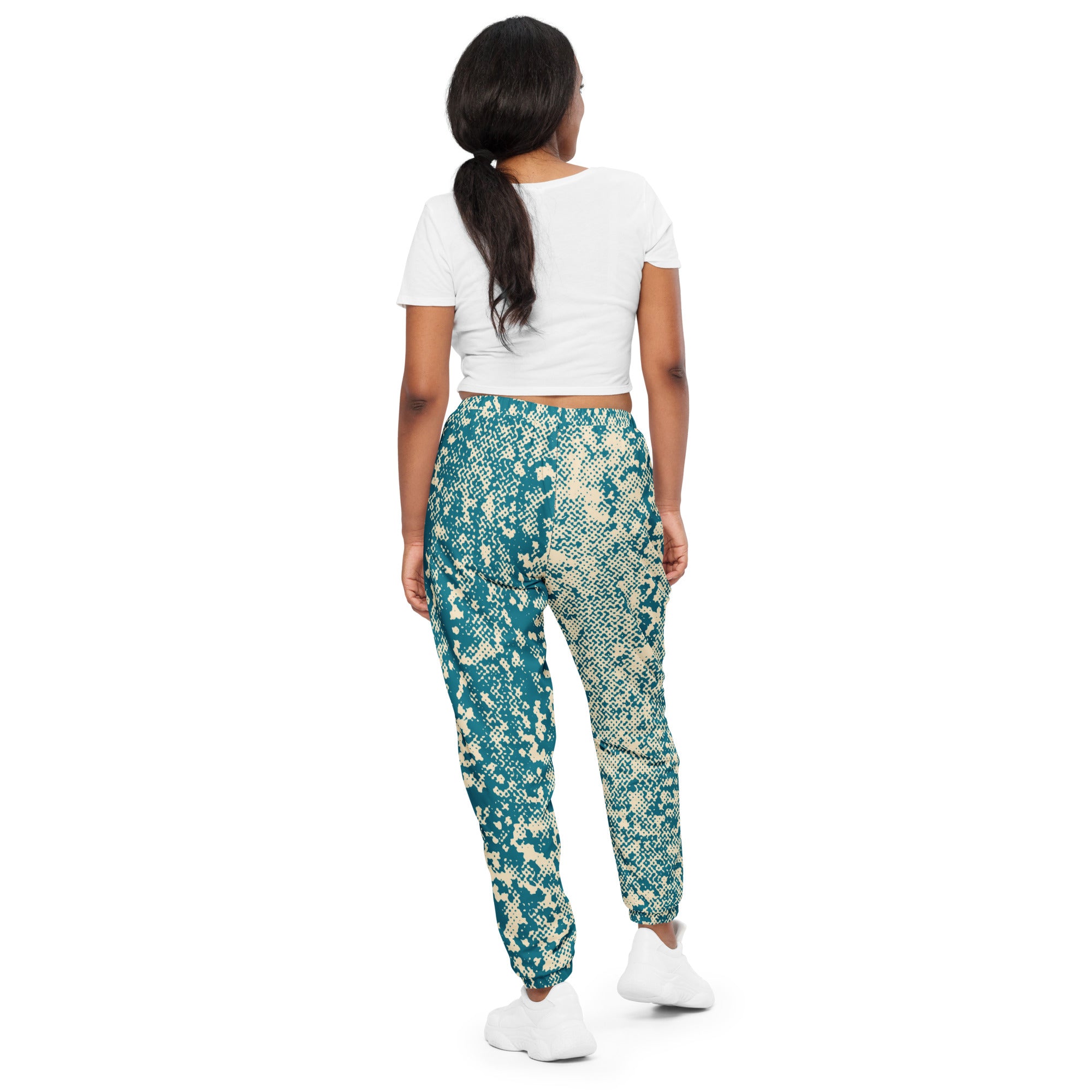 Person wearing a white crop top and teal patterned track pants on a white background