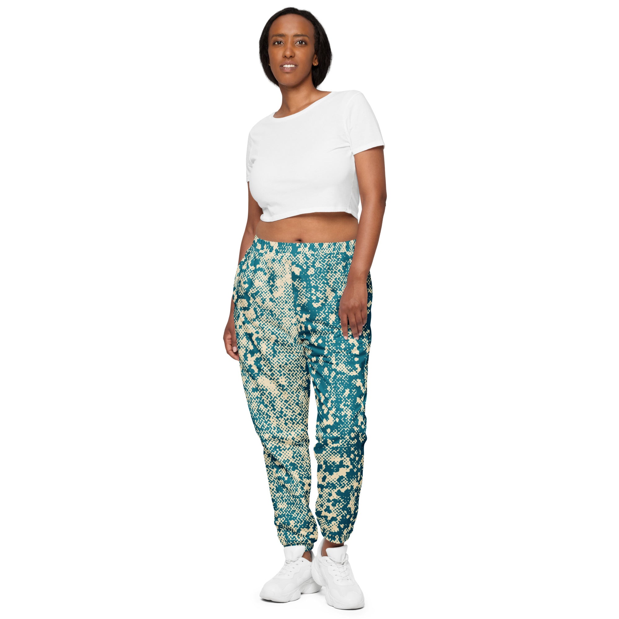 Woman wearing a white crop top and blue patterned track pants on a white background