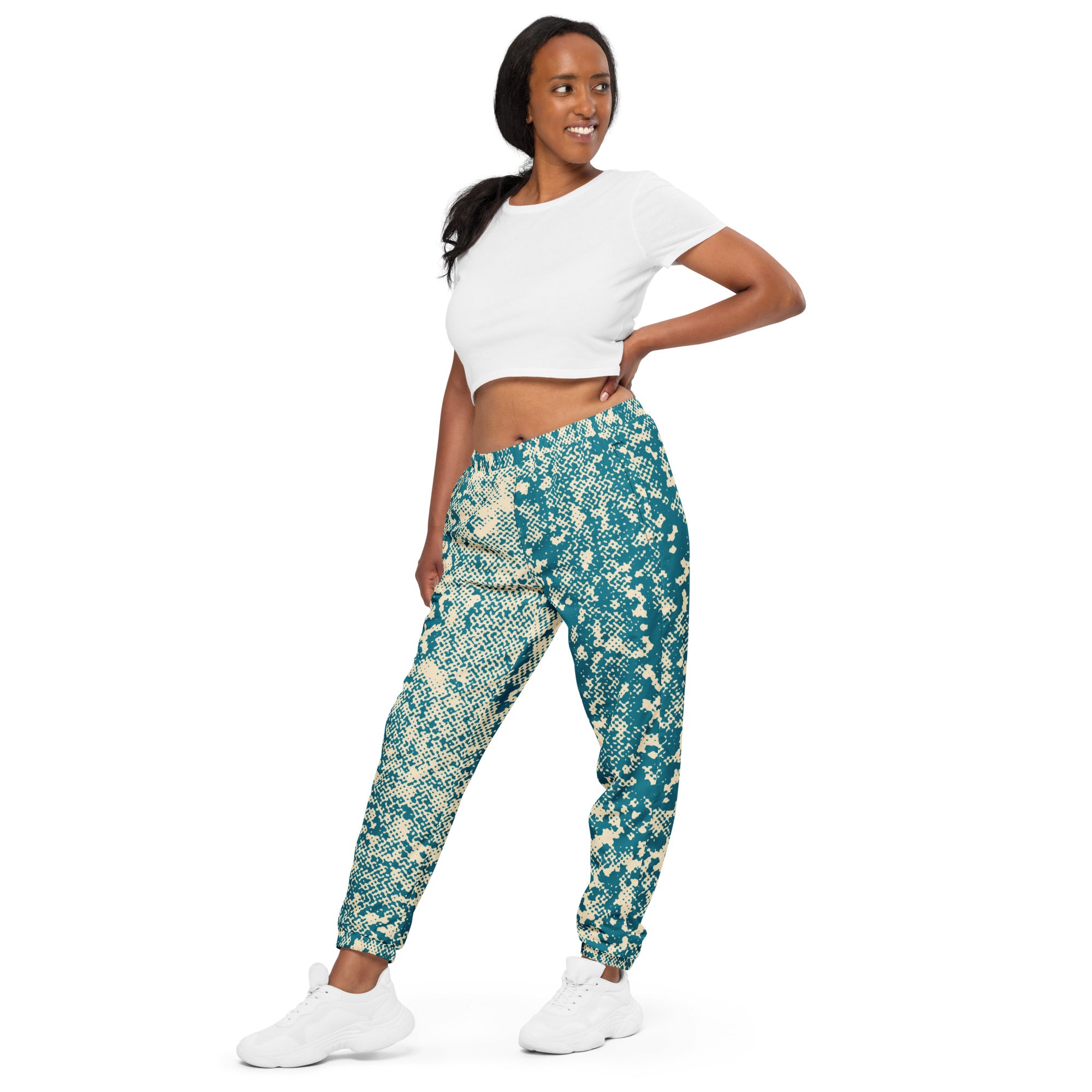Woman wearing teal and beige patterned track pants with a white top on a white background