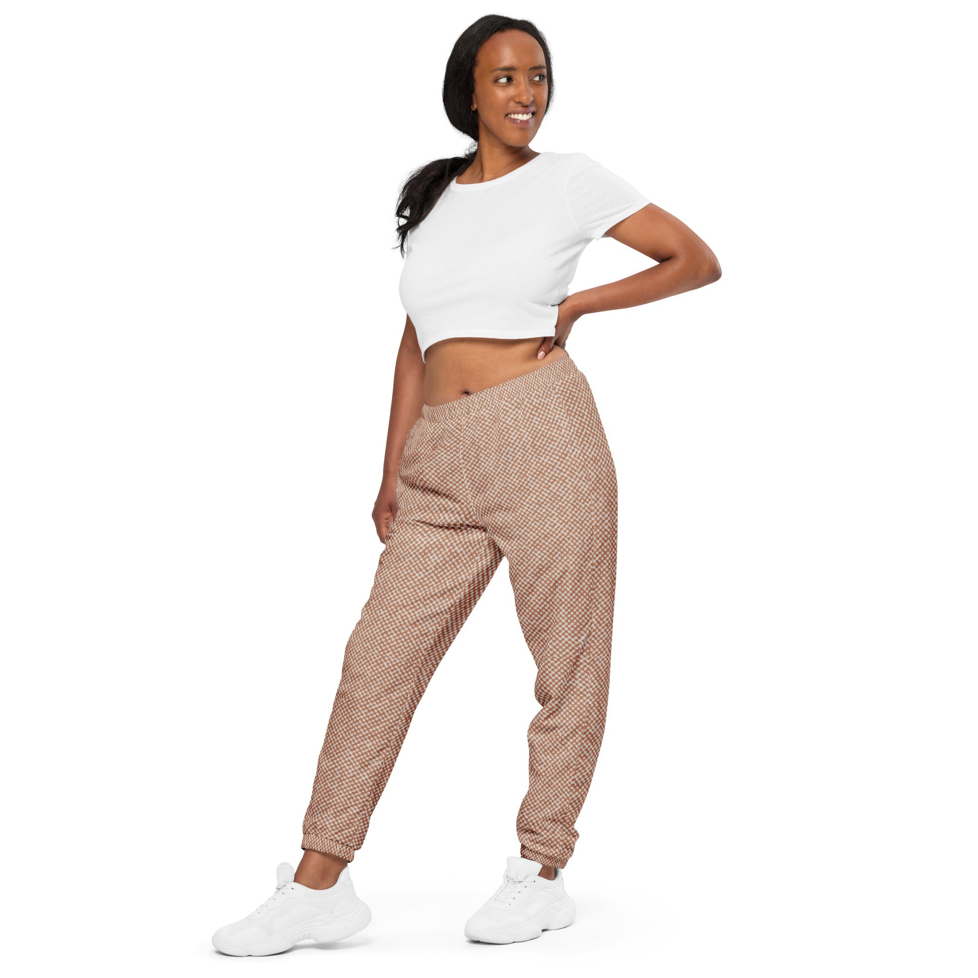 Woman wearing a white crop top and patterned track pants on a white background
