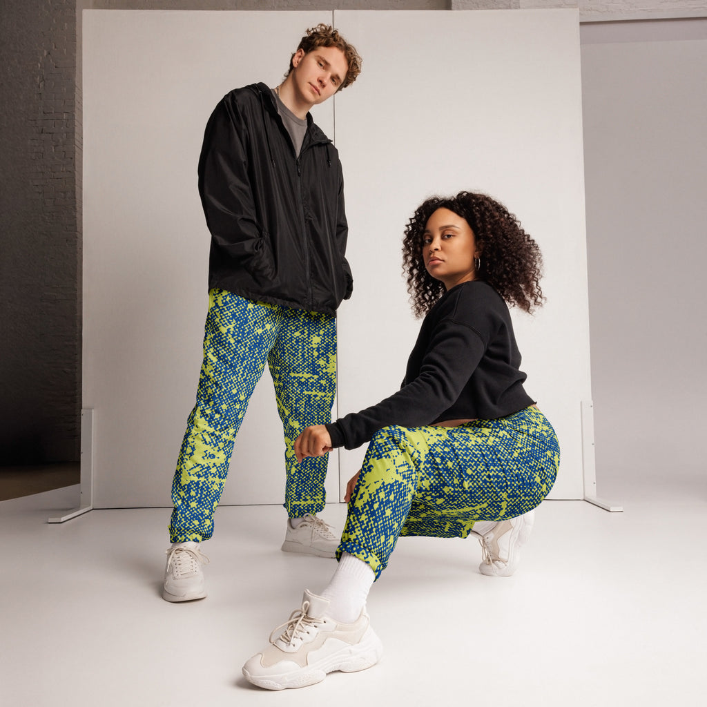 Two people wearing colorful patterned track pants in a studio setting.