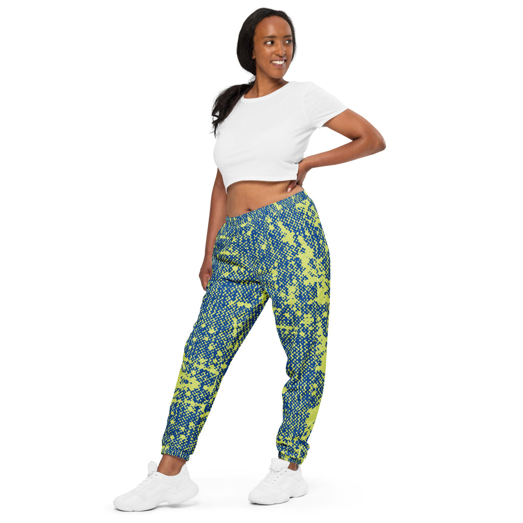 Side view of woman wearing a white crop top and blue and green patterned track pants on a white background