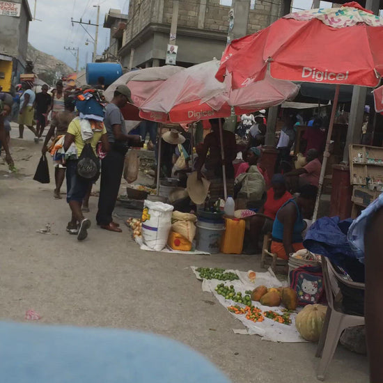 Mireille Fine Art, video detail showing a busy Haitian market in the afternoon, people passing by, others shopping and vendors selling food